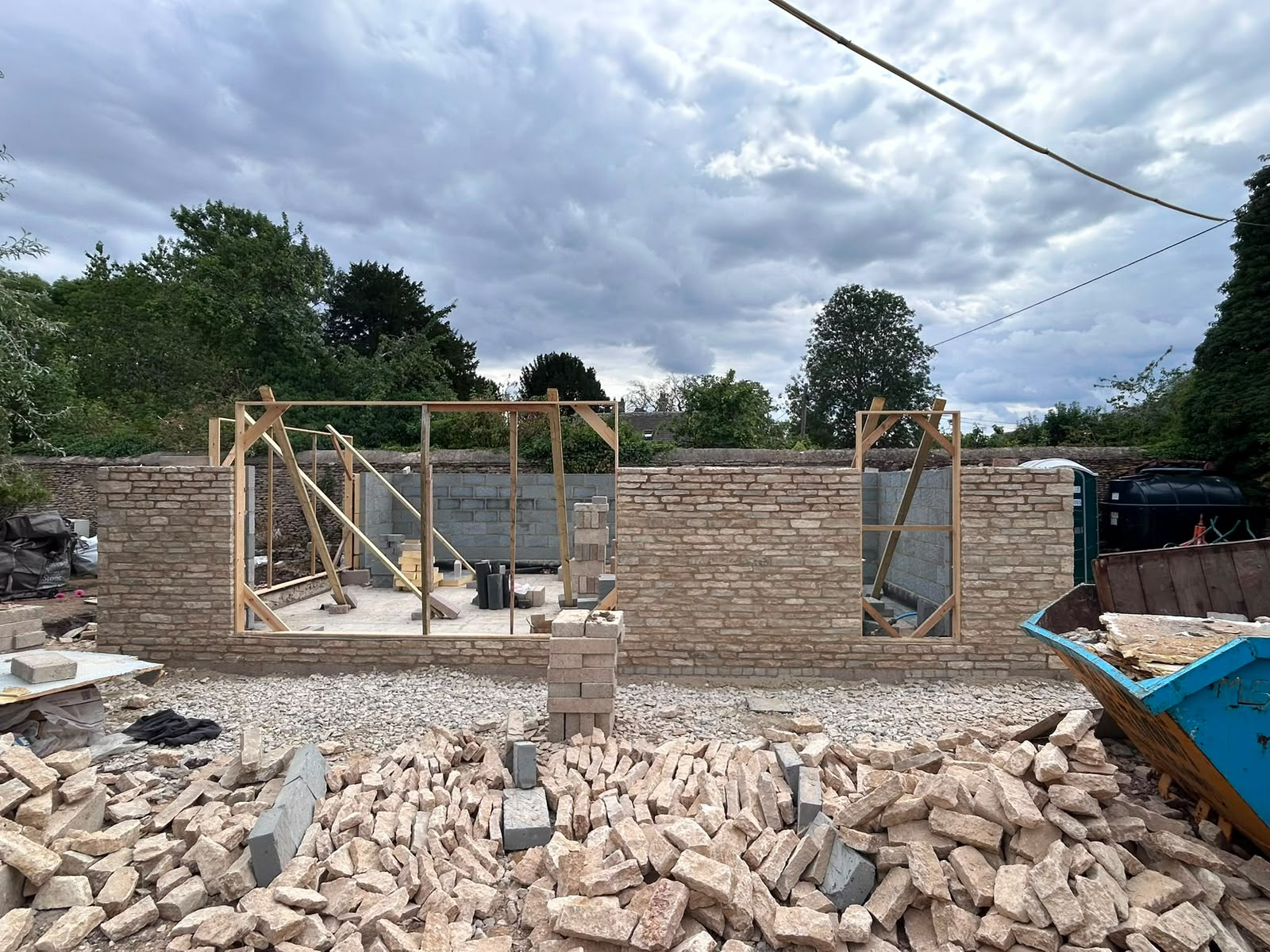 Cotswold stone garden walls under construction by DR Smith Building, with dressed stone openings framed for windows and reclaimed stone stacked on site.