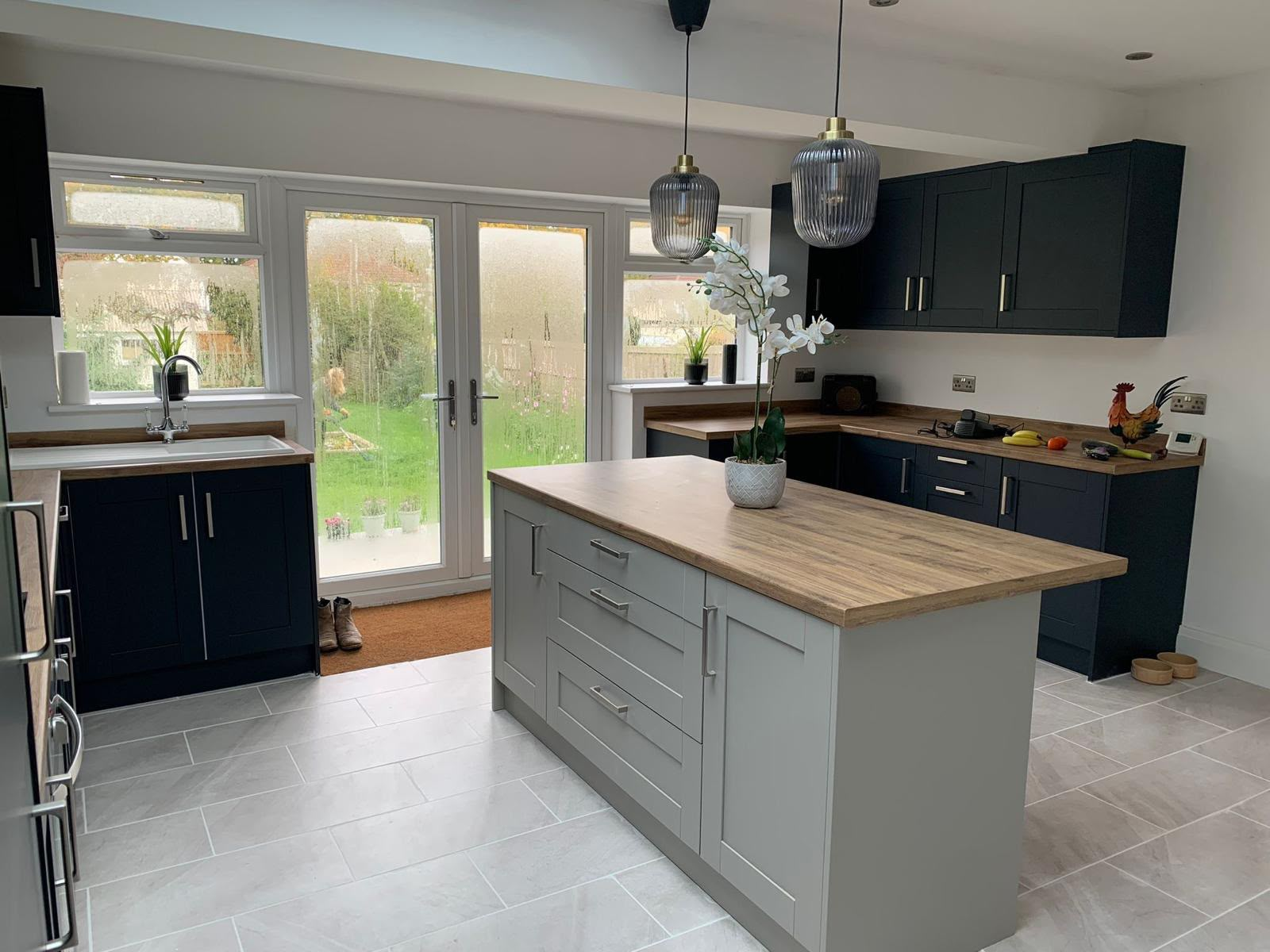Finished open-plan kitchen with navy shaker units, grey island, oak worktops and French doors to the garden, fitted by DR Smith Building.